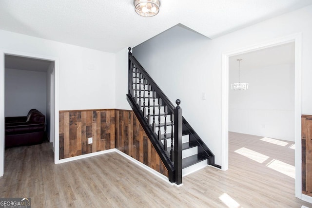 stairway featuring a notable chandelier, wooden walls, wainscoting, and wood finished floors