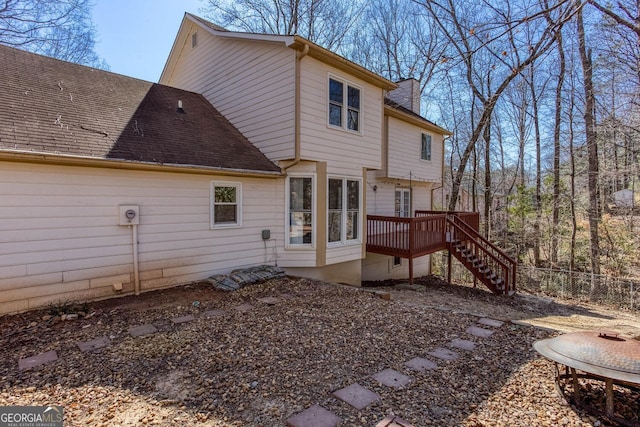 rear view of property with a deck, stairway, fence, and roof with shingles