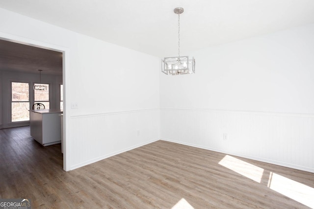 spare room with an inviting chandelier, wood finished floors, and wainscoting