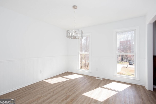 unfurnished dining area with a notable chandelier, visible vents, a healthy amount of sunlight, and wood finished floors