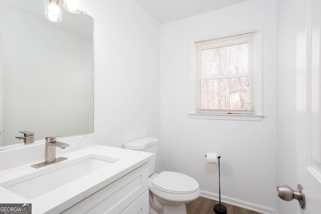 half bath with baseboards, toilet, wood finished floors, and vanity