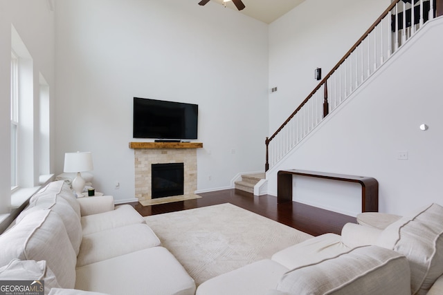 living area featuring stairway, a ceiling fan, wood finished floors, baseboards, and a high ceiling