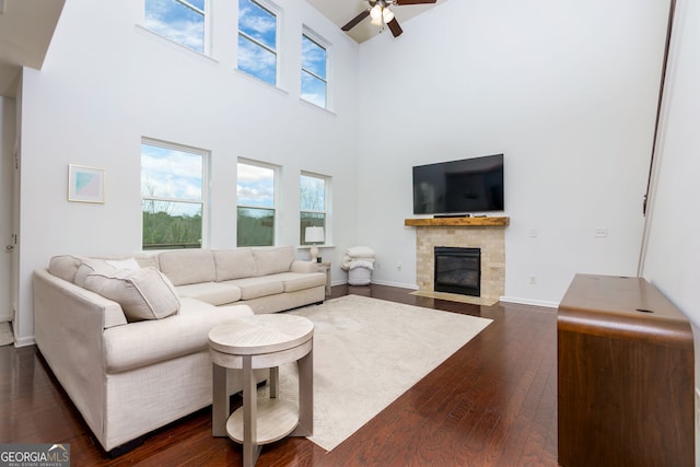 living room featuring ceiling fan, baseboards, dark wood finished floors, a tile fireplace, and a towering ceiling