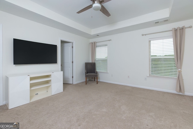 interior space featuring baseboards, visible vents, ceiling fan, a raised ceiling, and carpet flooring