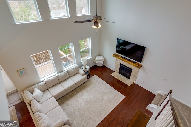 living area featuring a wealth of natural light, a tile fireplace, a towering ceiling, and wood finished floors