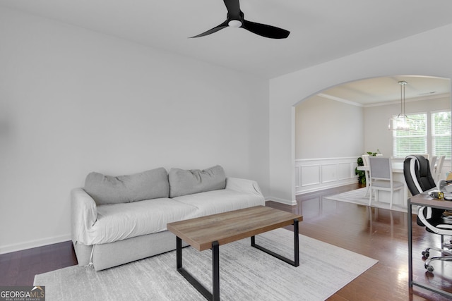 living area with a ceiling fan, a wainscoted wall, wood finished floors, arched walkways, and ornamental molding