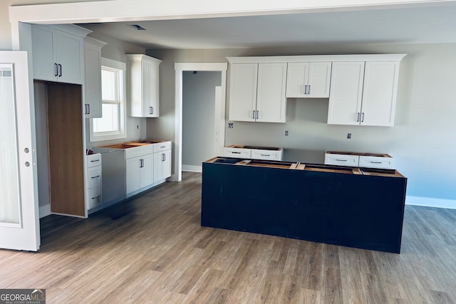 kitchen featuring white cabinetry, a kitchen island, baseboards, and wood finished floors