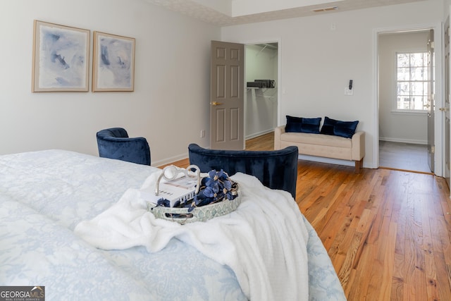 bedroom featuring light wood finished floors, a walk in closet, visible vents, and baseboards