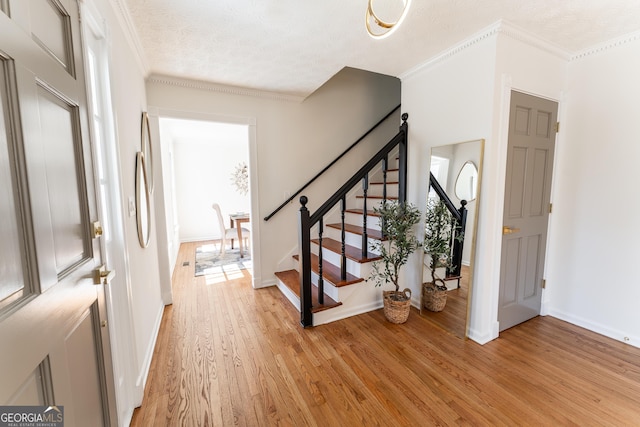 entrance foyer with a textured ceiling, light wood-style flooring, baseboards, ornamental molding, and stairway