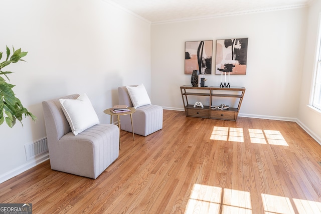 living area featuring ornamental molding, light wood-style flooring, visible vents, and baseboards