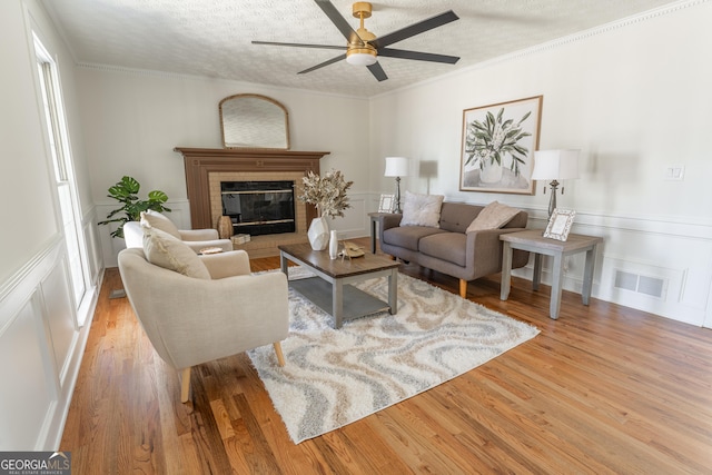 living area featuring crown molding, a fireplace, visible vents, a textured ceiling, and wood finished floors