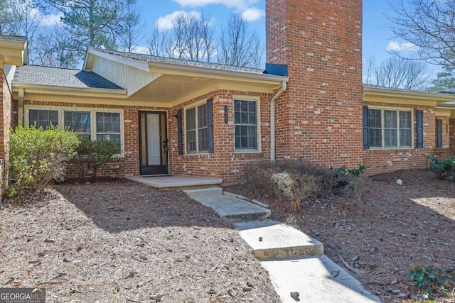 view of exterior entry featuring a chimney and brick siding