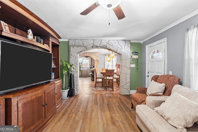 living area with arched walkways, ceiling fan, ornamental molding, a textured ceiling, and light wood-type flooring