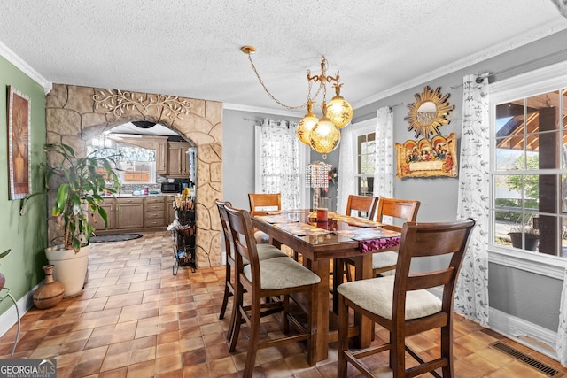 dining space with arched walkways, crown molding, visible vents, a textured ceiling, and baseboards