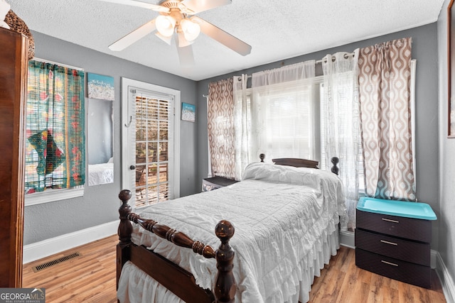 bedroom with a textured ceiling, wood finished floors, visible vents, and baseboards