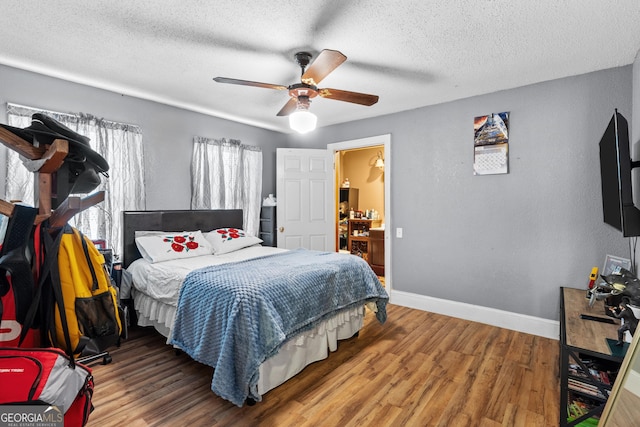 bedroom with a ceiling fan, a textured ceiling, baseboards, and wood finished floors