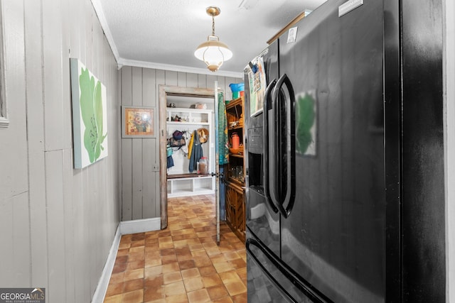 kitchen with a textured ceiling, wood walls, ornamental molding, black fridge, and pendant lighting