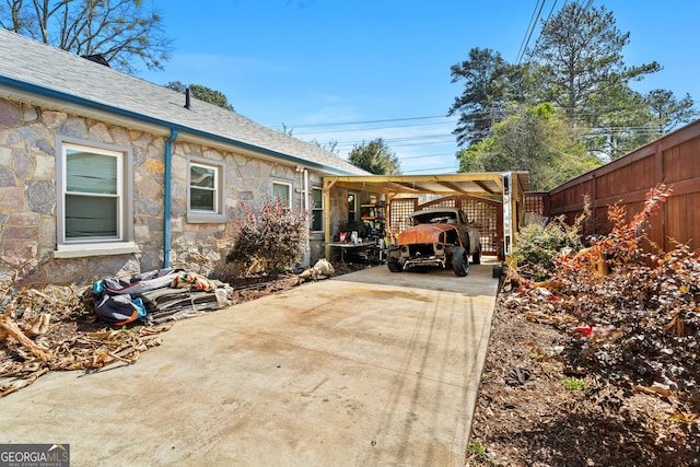 exterior space with roof with shingles, fence, an attached carport, stone siding, and driveway