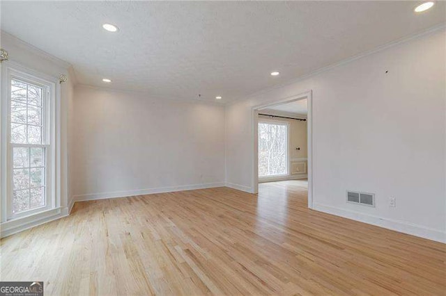 empty room with light wood-type flooring, baseboards, visible vents, and crown molding