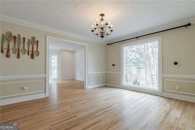 unfurnished dining area featuring light wood finished floors, crown molding, a chandelier, and a textured ceiling