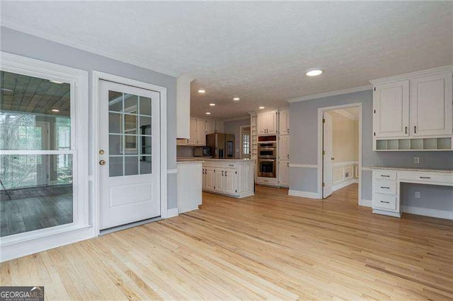 kitchen with stainless steel appliances, white cabinetry, light countertops, light wood-type flooring, and built in study area