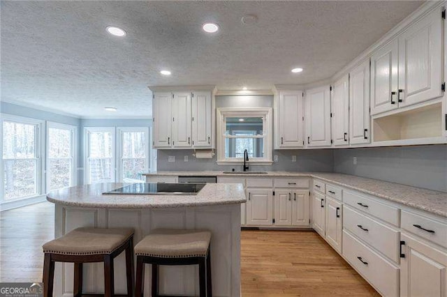 kitchen with a breakfast bar area, a sink, white cabinets, light wood-type flooring, and a wealth of natural light