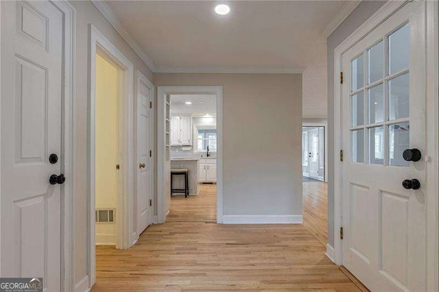 hallway featuring light wood-type flooring, visible vents, baseboards, and crown molding