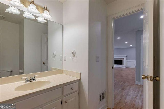 bathroom featuring visible vents, toilet, wood finished floors, vanity, and a fireplace