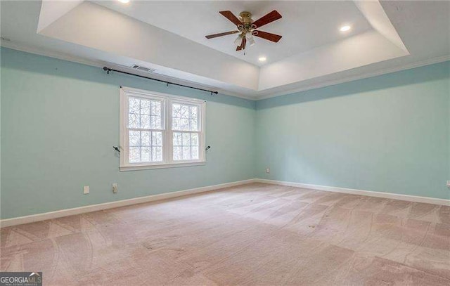 spare room featuring a tray ceiling, light colored carpet, and baseboards