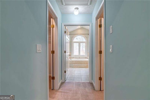 hall with light carpet, vaulted ceiling, and a textured ceiling