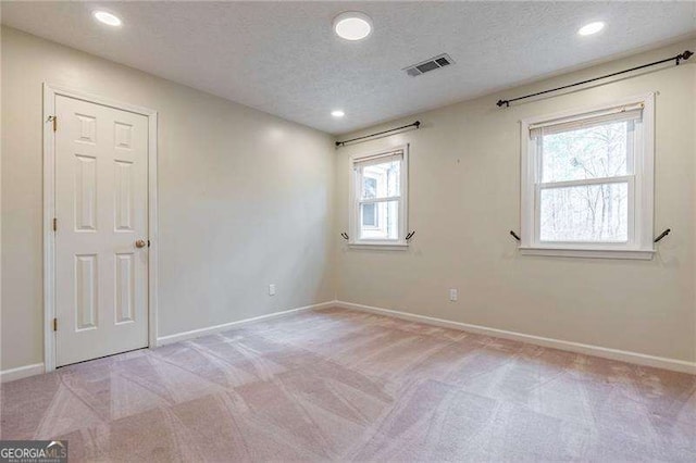 spare room featuring light carpet, baseboards, visible vents, and a textured ceiling