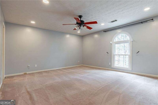 spare room with light colored carpet, visible vents, a ceiling fan, a textured ceiling, and baseboards