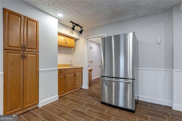 kitchen featuring a wainscoted wall, a textured ceiling, freestanding refrigerator, and wood tiled floor