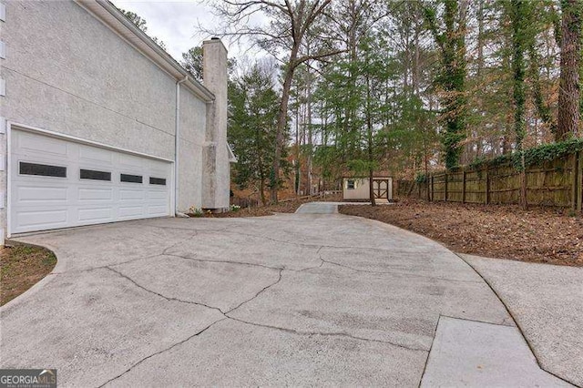 view of side of property featuring driveway, a garage, a chimney, fence, and stucco siding