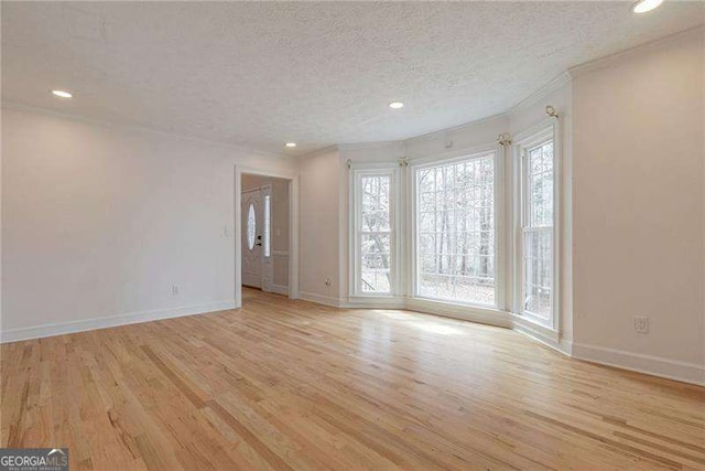 unfurnished room with light wood-style floors, baseboards, a textured ceiling, and ornamental molding