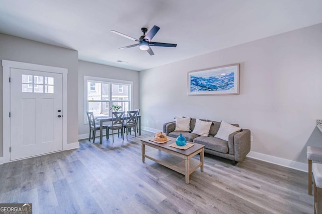 living room with a ceiling fan, baseboards, visible vents, and light wood finished floors