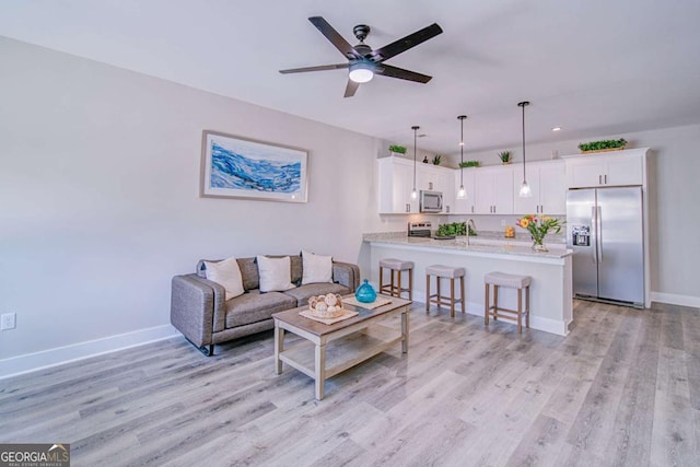 living area with light wood-type flooring, a ceiling fan, and baseboards