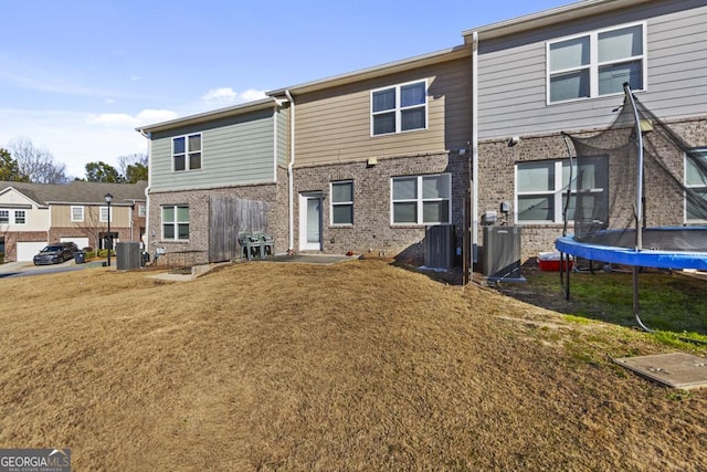 back of property featuring a trampoline, central AC unit, brick siding, and a lawn