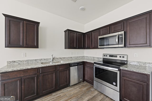 kitchen featuring light stone counters, light wood-style flooring, a sink, stainless steel appliances, and dark brown cabinetry