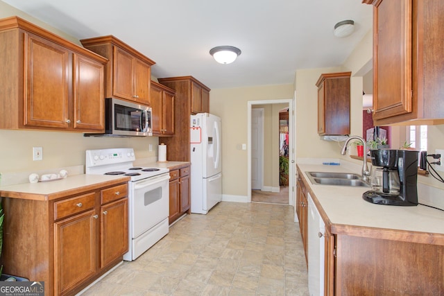 kitchen featuring white appliances, brown cabinetry, baseboards, a sink, and light countertops