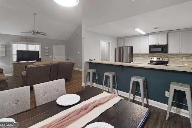 kitchen with decorative backsplash, dark wood-style floors, a breakfast bar, vaulted ceiling, and stainless steel appliances