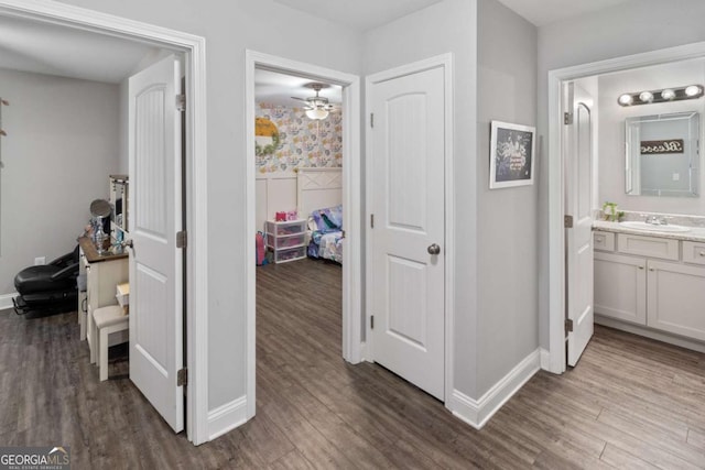 hall featuring dark wood-style floors, a sink, and baseboards