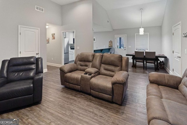 living room with high vaulted ceiling, wood finished floors, visible vents, and baseboards