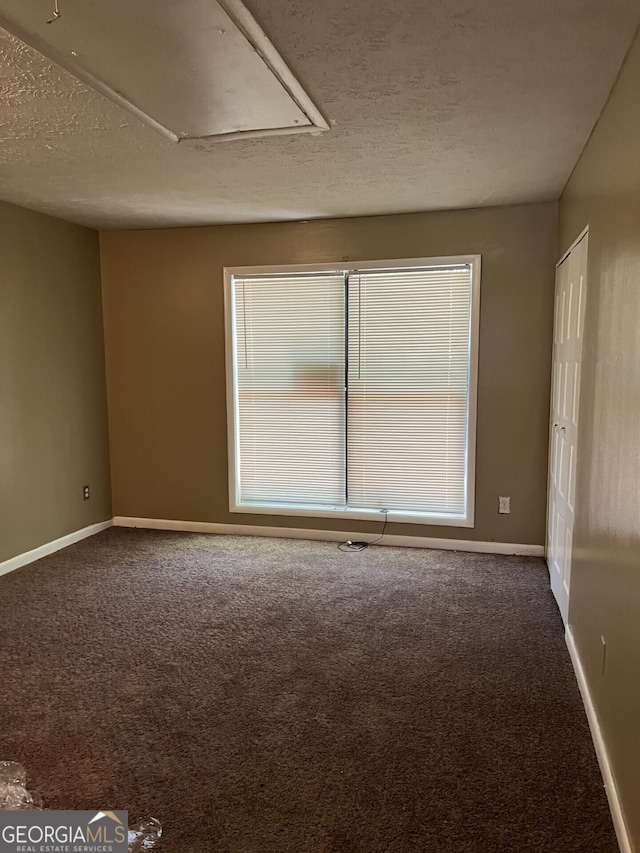 empty room with attic access, dark carpet, a textured ceiling, and baseboards