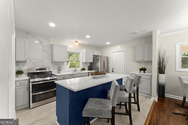 kitchen featuring backsplash, a breakfast bar area, light countertops, stainless steel appliances, and a sink