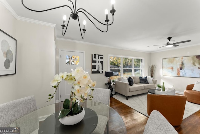 dining area with baseboards, ceiling fan with notable chandelier, wood finished floors, and ornamental molding