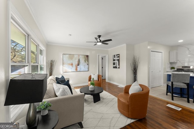 living area featuring crown molding, visible vents, light wood-type flooring, and baseboards