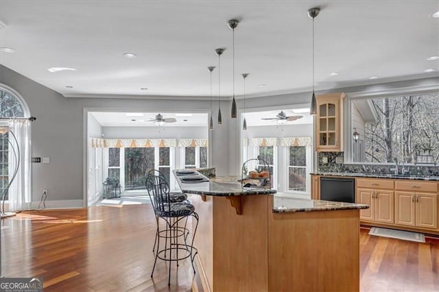 kitchen featuring wood finished floors, glass insert cabinets, dishwasher, a kitchen breakfast bar, and a wealth of natural light