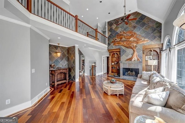 living area featuring high vaulted ceiling, a fireplace with raised hearth, ornamental molding, wood finished floors, and baseboards