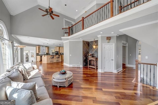 living area with ornamental molding, ceiling fan, baseboards, and wood finished floors